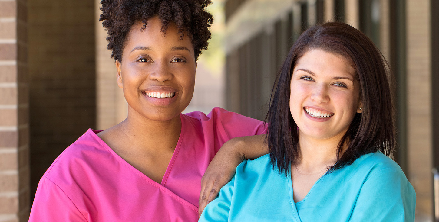 Two smiling female medical professionals standing side by side outdoors